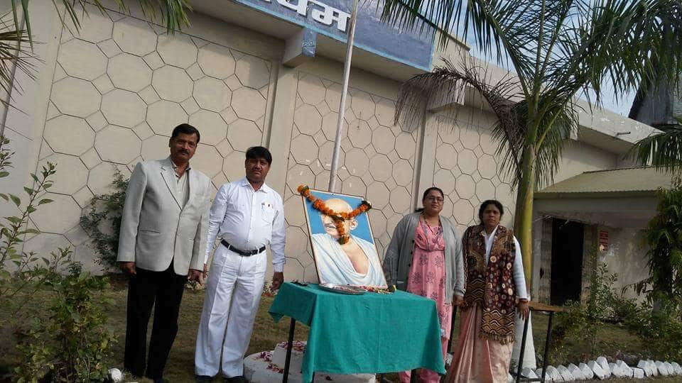 A photograph of staff of Mahatma Gandhi Homoeopathic Medical College taken while organising a medical camp, containing a photograph of Mahatma gandhi with a garland.